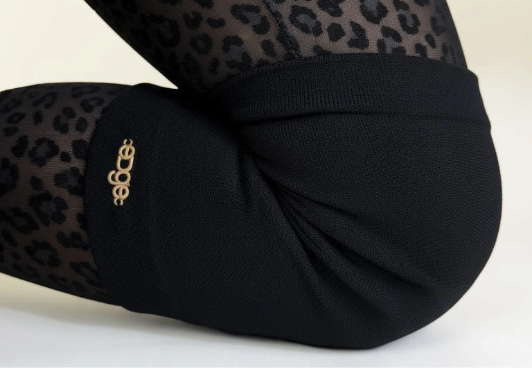 Black tights with leopard print pattern with black knee guards for figure skaters on a white background