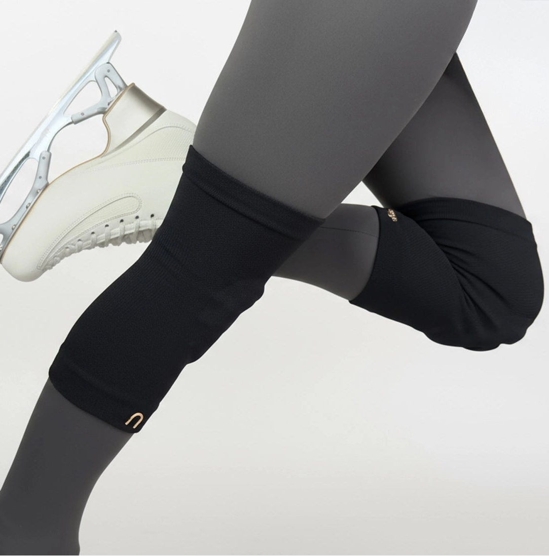 Figure skater wearing black leggings and black edge knee guards, with a white ice skate on a light gray background