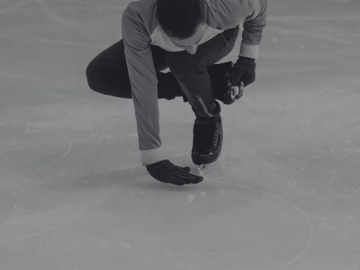 Figure skater adjusting gear on the ice wearing protective equipment.